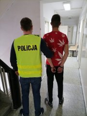 policjant w żółtej kamizelce z z napisem Policja prowadzi zatrzymanego do podpalenia auta mężczyznę