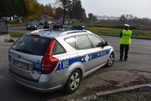 policjantka w żółtej kamizelce przy radiowozie kieruje ruchem na skrzyżowaniu w obrębie cmentarza